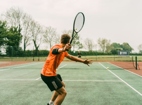 man in orange shirt and black shorts holding black and white tennis racket